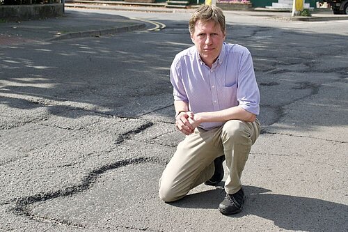 James MacCleary on one knee at the side of a pothole about five feet wide.