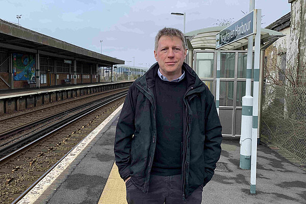 James MacCleary standing on the platform at Newhaven Harbour station. Behind him are empty tracks, station buildings and signalling paraphrenalia